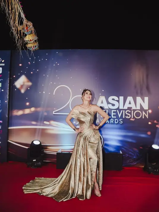 Gaun tersebut memiliki detail drapery yang rumit memberikan kesan mewah dan elegan. Gaunnya dipadukan dengan beberapa aksesoris emas seperti gelang dan anting besar yang mewah. @revashion, selaku fashion stylist, berhasil mengkurasi gaya yang menonjolkan pesona Luna dengan sempurna.  [@styledbyrevashion/@lunamaya].