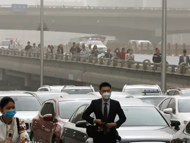 Warga mengenakan masker melewati kendaraan yang terjebak kemacetan saat badai debu di jalanan Beijing, Kamis (4/5). Badai debu menerjang utara China dan Beijing, serta membuat otoritas membatalkan puluhan penerbangan. (AP Photo/Andy Wong)