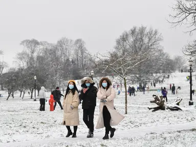 Orang-orang yang mengenakan masker berjalan di atas salju di Primrose Hill di London saat ibu kota mengalami hujan salju yang jarang terjadi pada Minggu (24/1/2021). Hujan salju langka itu membawa kegembiraan di tengah penguncian atau penutupan wilayah (lockdown) secara nasional. (JUSTIN TALLIS/AFP)