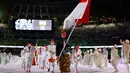 Peselancar Indonesia Rio Waida membawa bendera Merah-Putih saat defile upacara pembukaan Olimpiade Tokyo 2020, di Stadion Nasional Jepang, Tokyo, Jumat malam (23/7/2021). Kontingen Indonesia mengenakan kaus merah dengan dibalut jas dan celana putih. (Ben STANSALL/AFP)