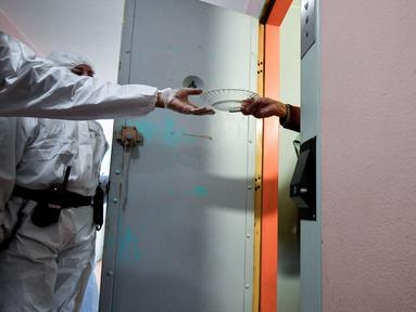 Seorang narapidana (kiri) yang mengenakan APD diawasi penjaga saat membagikan makanan siang kepada para tahanan di sel mereka sebagai bagian dari langkah-langkah mengekang penyebaran Covid-19 di pusat-pusat penahanan, di penjara Villepinte, dekat Paris, pada 6 Januari 2022. (ALAIN JOCARD/POOL/AFP)