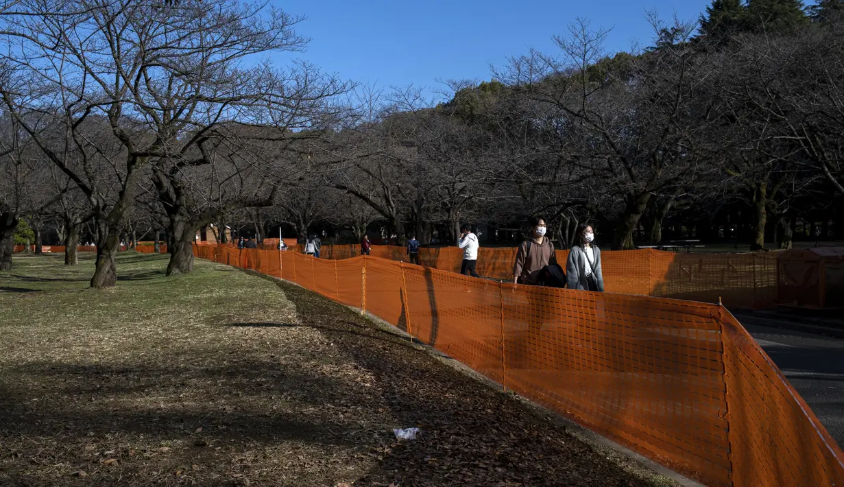 Orang-orang melewati jalan setapak di antara pagar yang ditempatkan untuk mencegah pesta melihat bunga sakura (Hanami) untuk pencegahan COVID-19 di Tokyo (13/3/2021).  Pemerintah Jepang tengah memperpanjang keadaan darurat di wilayah Tokyo hingga 21 Maret. (AP Photo/Kiichiro Sato)