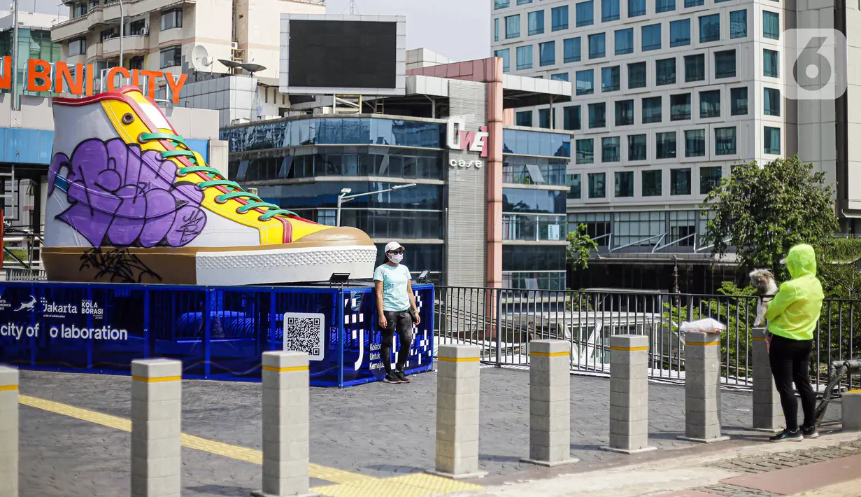 Warga berfoto di depan Tugu Sepatu, Sudirman, Jakarta, Minggu (19/9/2021). Tugu Sepatu menjadi sasaran pencoretan dengan semprotan aerosol oleh orang tak dikenal sehari usai diresmikan pada 17 September 2021. (Liputan6.com/Faizal Fanani)