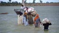Sebuah keluarga pengungsi mengarungi daerah banjir setelah hujan deras, di Jaffarabad, sebuah distrik di provinsi Baluchistan barat daya Pakistan, Rabu (24/8/2022). Hujan deras telah memicu banjir bandang dan mendatangkan malapetaka di banyak tempat. (AP Photo/Zahid Hussain)