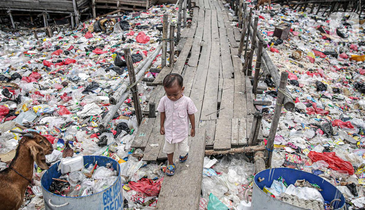 Seorang anak berjalan di jembatan kayu di antara sampah di perkampungan nelayan Cilincing, Jakarta, Minggu (21/2/2022). Peringatan HPSN 2022, Pemprov DKI Jakarta mengajak warga Jakarta peduli sampah mulai dari lingkungan terdekat dengan cara memilah sampah dari rumah. (Liputan6.com/Faizal Fanani)
