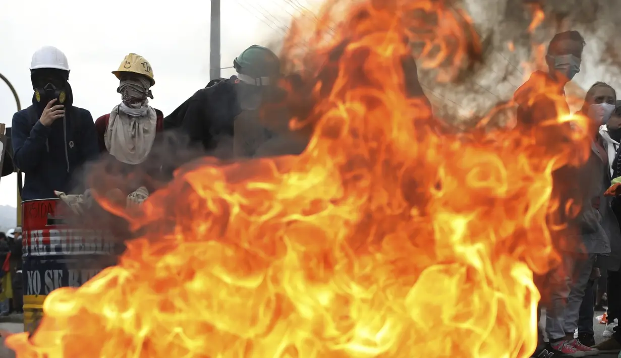 Pengunjuk rasa berdiri dengan perisai di sekitar barikade yang terbakar selama protes anti-pemerintah di Bogota, Kolombia (28/5/2021). Warga Kolombia telah turun ke jalan selama berminggu-minggu setelah pemerintah mengusulkan kenaikan pajak. (AP Photo/Ivan Valencia)