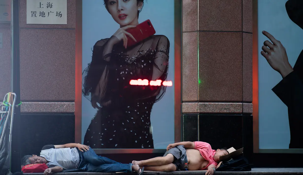 Dua pria tidur di depan sebuah pusat perbelanjaan di sepanjang Nanjing East Road, Shanghai (8/8). Penduduk setempat mencoba untuk mengalahkan panas rumah mereka dengan tidur di luar di bangku atau trotoar. (AFP Photo/Johannes Eisele)