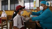 Petugas mengukur suhu seorang siswa sebelum mengikuti vaksinasi covid-19 di SDN Panunggangan 5, Pinang, Kota Tangerang, Selasa (19/10/2021).  Pelaksanaan vaksinasi untuk pelajar usia 12 tahun ini dilakukan dalam rangka persiapan pelaksanaan pembelajaran tatap muka (PTM). (Liputan6.com/Angga Yuniar)