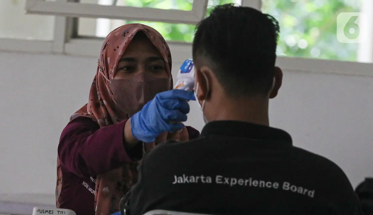 Petugas kesehatan mengecek suhu tubuh tenaga kesehatan relawan yang bertugas di RSDC, Wisma Atlit, Kemayoran, Jakarta. Rabu (3/8/2022). Pemberian vaksinasi Covid-19 dosis booster ke-2 tersebut diberikan dengan interval 6 bulan sejak vaksinasi dosis booster pertama. (Liputan6.com/Faizal Fanani)