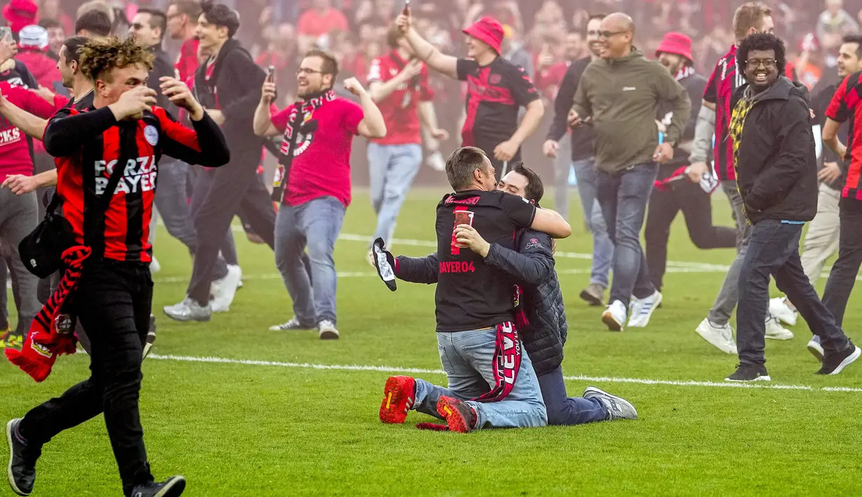 Dua orang suporter Bayer Leverkusen berpelukan saat merayakan keberhasilan timnya menjuarai Liga Jerman 2023/2024 setelah mengalahkan Werder Bremen di BayArena, Leverkusen, Jerman, Senin (15/04/2024) WIB. (AP Photo/Martin Meissner)