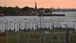 Para pemain bertanding sepak bola selama matahari terbenam di Brooklyn Bridge Park, New York City, Amerika Serikat, 20 Mei 2018. Olahraga semakin berkesan dengan latar belakang Patung Liberty. (HECTOR RETAMAL/AFP)