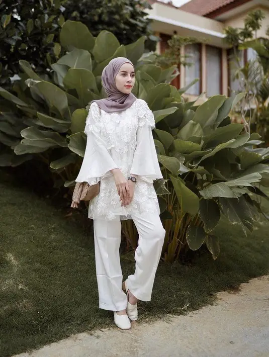 Perpaduan celana kulot dengan atasan blouse lengan lonceng warna putih bikin tampilan kondangan kian memesona. Tambahkan pula hijab pashmina warna lebih gelap dan heels. (Instagram/emyaghnia).