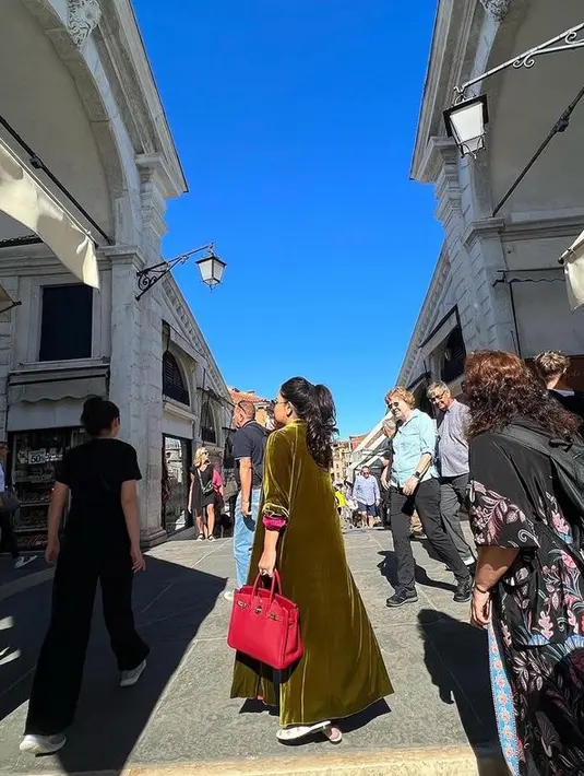 Mayang tak segan memakai warna-warna berani kala berada di Venesia. Ia santai memadukan hijau lumut dengan tas merah membara. (instagram.com/mayangsari_official)