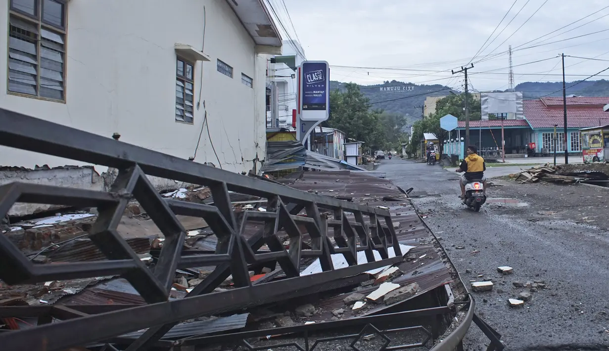 Pengendara motor melewati sebuah gedung yang rusak akibat gempa bumi di Mamuju, Sulawesi Barat, Sabtu (16/1/2021). Jalan dan jembatan yang rusak, pemadaman listrik, dan kurangnya alat berat menghambat evakuasi setelah gempa bermagnitudo 6,2 SR yang melanda Majene- Mamuju. (AP Photo/Azhari Surahman)