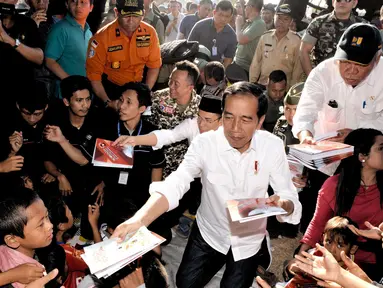 Presiden Joko Widodo atau Jokowi bersama Gubernur NTB Tuan Guru Bajang (TGB) Zainul Majdi membagikan buku saat mengunjungi korban gempa di lapangan Desa Madayin, Sambelia, Lombok Timur, NTB, Senin (30/7). (Agus Suparto/Indonesian Presidential Palace/AFP)