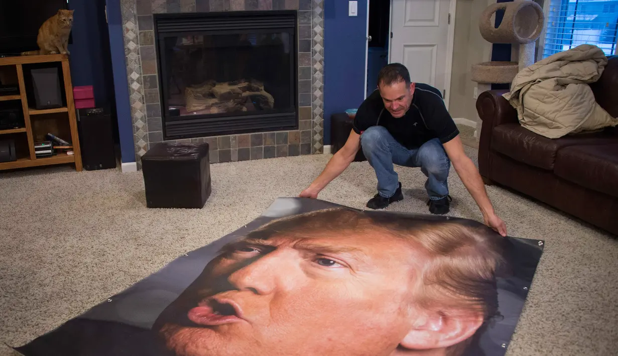 George Davey, pendukung calon Presiden AS Donald Trump membentangkan poster berukuran besar diruang tamu rumahnya untuk mengantikan poster trump yang pernah dirusak dihalaman belakang rumahnay di West Des Moines, Iowa, (25/1/2016). (AFP/JIM WATSON)