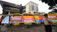 Petugas mengecek ponsel di dekat karangan bunga yang diletakkan di depan Museum Polri, Jakarta, Rabu (3/5). Ratusan karangan bunga itu terus berdatangan dan mengelilingi gedung Mabes Polri di Jalan Trunojoyo Jakarta. (Liputan6.com/Helmi Fithriansyah)