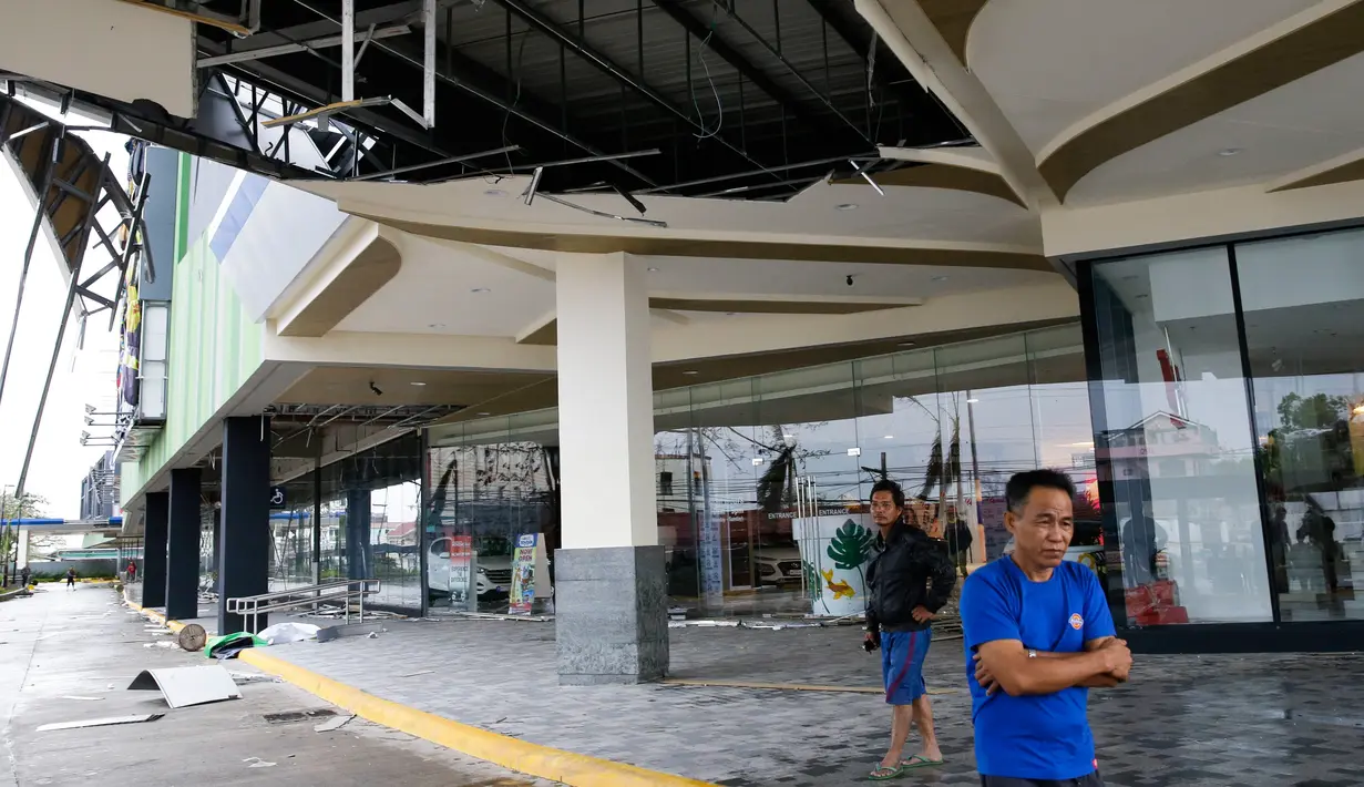 Warga berdiri di sebuah mal yang rusak akibat diterjang angin kencang dari Topan Mangkhut di kota Tuguegarao di provinsi Cagayan, Filipina timur laut (15/9). Topan Mangkhut diperkirakan akan berembus menuju bagian utara Filipina. (AP Photo/Aaron Favila)