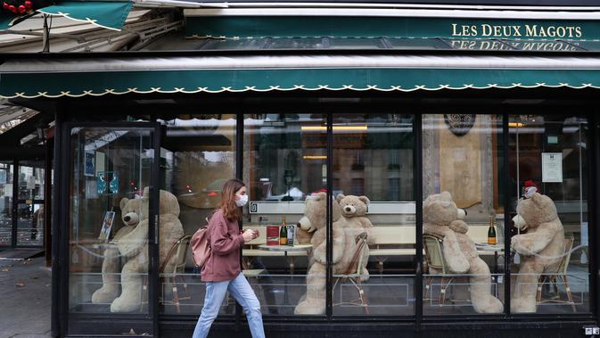 Pejalan kaki melintas di depan boneka beruang raksasa di kafe Les Deux Magots yang ditutup di Paris, Prancis, pada 16 Desember 2020. Boneka beruang itu dipajang untuk menggantikan pengunjung saat restoran tutup selama penerapan jam malam guna menekan laju penyebaran COVID-19. (Xinhua/Gao Jing)