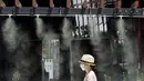 Seorang wanita berjalan di bawah titik kabut yang menyejukkan di sepanjang jalan di Tokyo, Selasa (10/8/2021). Menurut biro meteorologi Jepang, cuaca panas panas terus berlanjut di wilayah metropolitan saat suhu naik menjadi 338 derajat Celcius (100,4 derajat Fahrenheit). (AP Photo/Eugene Hoshiko)