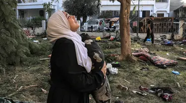 Seorang wanita bereaksi sambil memegang bantal ketika dia berdiri di tengah puing-puing di luar lokasi rumah sakit Ahli Arab di Gaza tengah pada 18 Oktober 2023. (MAHMUD HAMS/AFP)