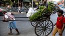 Seorang pria duduk di atas becak yang ditarik dengan tangan membawa pisang dan bahan-bahan lain untuk ibadah menjelang festival Hindu Chhat, di Kolkata, India (9/11/2021). (AP Photo/Bikas Das)