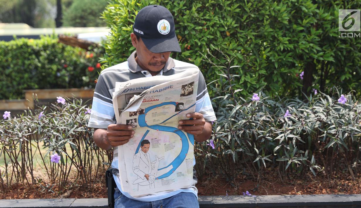 Warga membaca koran di TMP Kalibata untuk melihat prosesi pemakaman Presiden RI ke-3 BJ Habibie, Jakarta, Kamis (12/9/2019). BJ Habibie wafat pada Rabu (11/9) di usia 83 tahun. (Liputan6.com/Helmi Fithriansyah)