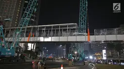 Petugas menggunakan alat berat merobohkan Jembatan Penyebrangan Orang (JPO) di Kawasan Bundaran HI, Jakarta, Senin (30/7/2018) malam. Pembongkaran JPO ini juga terkait upaya mempercantik ibu kota jelang Asian games 2018. (Liputan6.com/Herman Zakharia)
