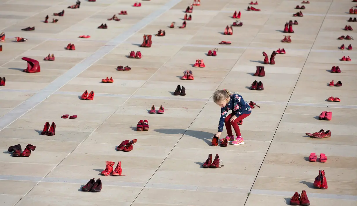 Seorang anak di antara instalasi ratusan sepatu merah untuk memprotes kekerasan terhadap perempuan di Habima Square, Tel Aviv, Selasa (4/12). Sepanjang tahun ini, 24 perempuan Israel tewas akibat tindakan kekerasan dalam rumah tangga. (AP/Oded Balilty)