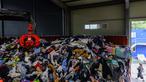 Dalam foto yang diambil pada tanggal 7 Agustus 2024 memperlihatkan seorang karyawan berjalan melewati gudang yang berisi tumpukan besar garmen, tempat tidur, mainan lunak, dan aksesori yang dikategorikan dengan cakar mekanis, sebelum diekspor ke luar negeri, di pabrik pakaian bekas di Paju, sekitar 28 km sebelah utara Seoul, Korea Selatan. (ANTHONY WALLACE/AFP)