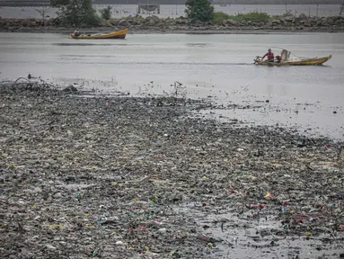 Nelayan melintas di dekat tumpukan sampah laut di muara Kanal Timur di Marunda Kepu, Cilincing, Jakarta, Kamis (8/6/2023). (Liputan6.com/Faizal Fanani)