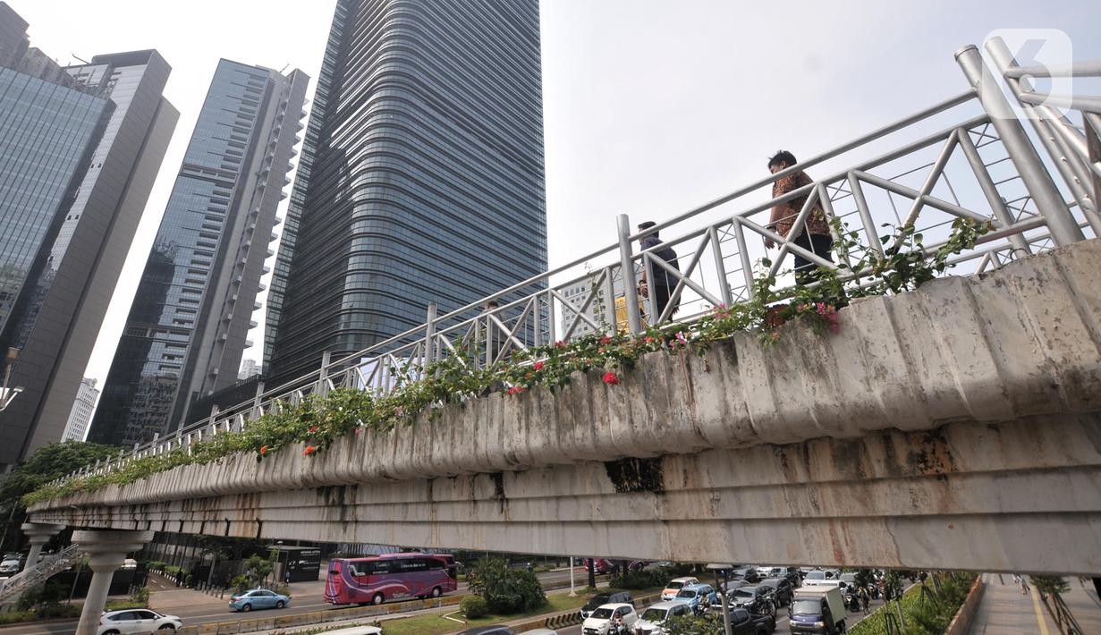 Pejalan kaki melintas di jembatan penyeberangan orang (JPO) yang tidak beratap di jalan Sudirman, Jakarta, Rabu (6/11/2019). Pemprov DKI melalui Dinas Bina Marga mencopot atap JPO Sudirman agar pejalan kaki dapat menikmati pemandangan gedung-gedung pencakar langit. (merdeka.com/Iqbal Nugroho)