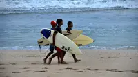 Anak-anak berjalan dengan papan selancar mereka di pantai Kuta di pulau resor Bali (4/10/2021). Pemerintah akan menyiapkan hotel-hotel yang dipersiapkan untuk karantina. (AFP/Sony Tumbelaka)