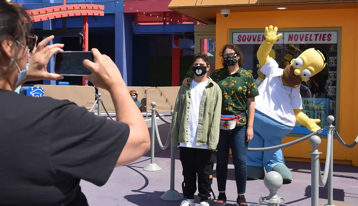 Para tamu berpose dengan Homer Simpson pada hari pembukaan pemegang tiket musiman dan tahunan Universal Studios di Los Angeles, California, Kamis (15/4/2021). Universal Studios Hollywood akan dibuka kembali pada 16 April setelah lebih dari setahun tutup karena Pandemi covid-19. (LISA O'CONNOR/AFP)
