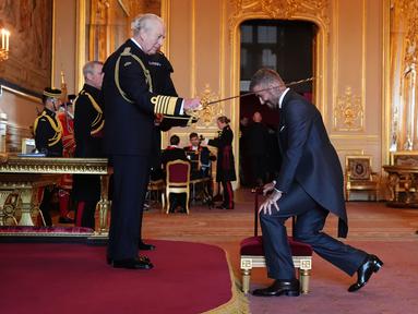 Mantan pesepak bola, David Beckham (kanan) dianugerahi gelar Ksatria oleh Raja Inggris, Charles III dalam upacara penobatan di Kastil Windsor, Berkshire, Inggris, Selasa (04/11/2025) waktu setempat. (AP Photo/PA/Jonathan Brady)