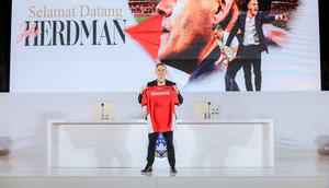 Pelatih baru Timnas Indonesia, John Herdman, berpose dengan menunjukkan jersey merah Skuad Garuda dalam konferensi pers perkenalannya di Hotel Mulia, Jakarta, Selasa (13/1/2026). (Bola.com/Bagaskara Lazuardi)