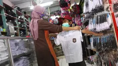 Pembeli mencoba seragam sekolah baru kepada anaknya di salah satu toko di Tangerang, Banten, Selasa (2/6/2020). Menjelang tahun ajaran baru, sejumlah pedagang di tempat tersebut mengeluh karena omzet penjualan seragam sekolah menurun drastis akibat pandemi COVID-19. (Liputan6.com/Angga Yuniar)