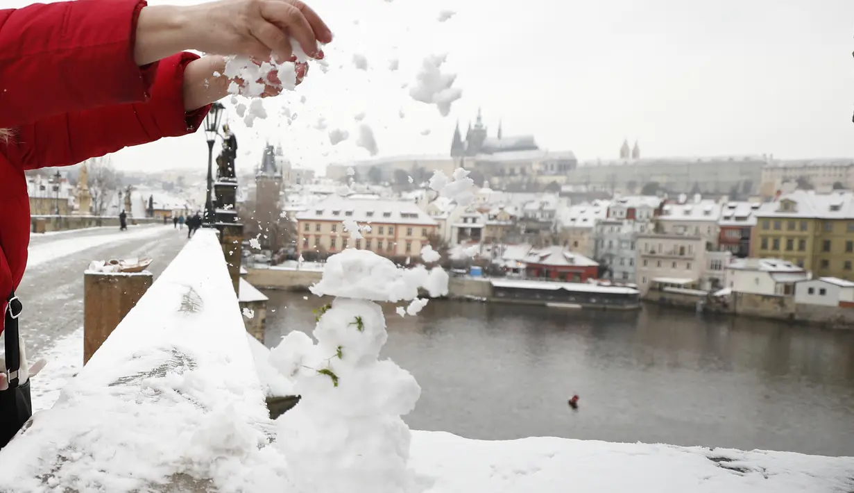 Seorang wanita menaburkan es ke manusia salju di Jembatan Charles abad pertengahan setelah hujan salju pertama di Praha, Republik Ceko (3/12/2020). (AP Photo / Petr David Josek)