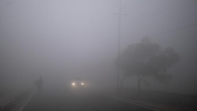 Sebuah mobil dengan lampu depan melaju melewati jalan yang diselimuti kabut tebal pada pagi yang dingin di pinggiran New Delhi, India (1/1/2021). Di sisi lain, Madhya Pradesh di India tengah mendapat kelegaan dari dingin yang menggigit karena merkuri naik beberapa tingkat. (AP Photo/Altaf Qadri)
