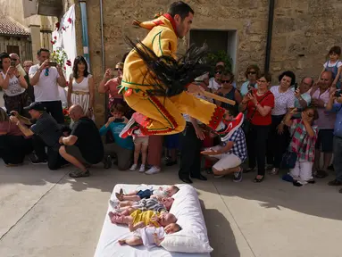 Pria berkostum setan melompati bayi-bayi yang terlentang di atas matras di sebuah jalan selama festival El Colacho di desa Castrillo de Murcia, bagian utara Spanyol, 23 Juni 2019. Festival melompati bayi ini sudah menjadi perayaan tahunan sejak tahun 1620. (CESAR MANSO/AFP)