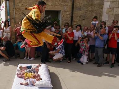 Pria berkostum setan melompati bayi-bayi yang terlentang di atas matras di sebuah jalan selama festival El Colacho di desa Castrillo de Murcia, bagian utara Spanyol, 23 Juni 2019. Festival melompati bayi ini sudah menjadi perayaan tahunan sejak tahun 1620. (CESAR MANSO/AFP)