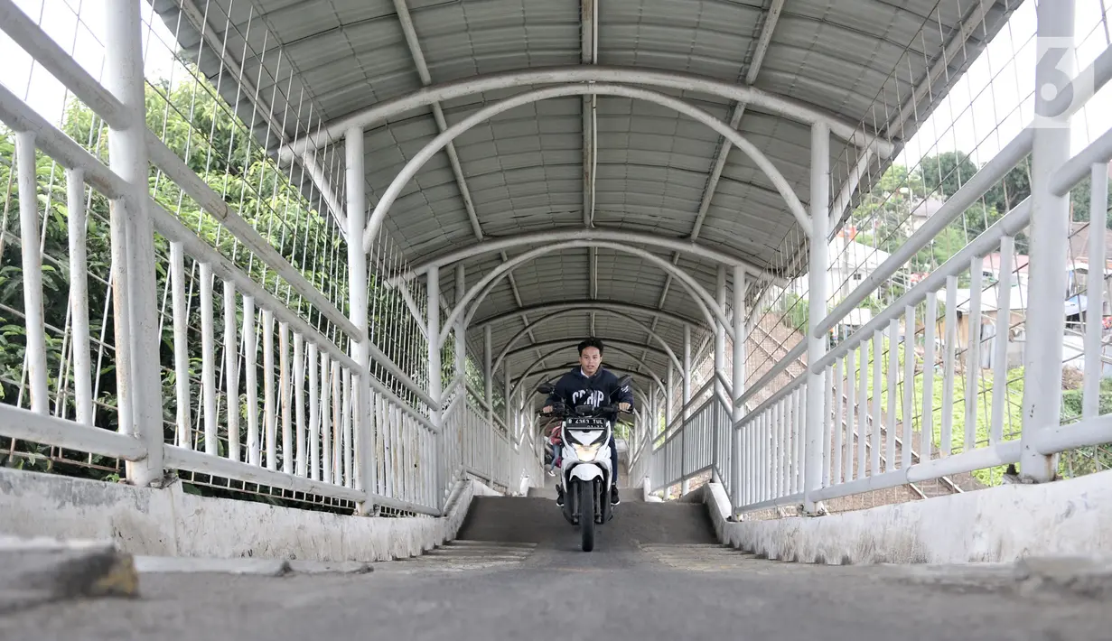 Pengendara sepeda motor melintasi jembatan penyeberangan orang (JPO) Stasiun Pasar Minggu Baru, Jakarta, Selasa (10/3/2020). JPO tersebut kerap disalahgunakan pengendara motor sebagai jalan alternatif untuk mempersingkat jarak tempuh meski rambu larangan sudah dipasang. (merdeka.com/Iqbal Nugroho)