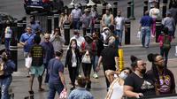 Pejalan kaki dengan masker dan tanpa masker berjalan di sepanjang Las Vegas Strip, di Las Vegas Selasa (27/4/2021). Warga Amerika Serikat (AS) yang telah menerima vaksin COVID-19 tidak lagi diwajibkan mengenakan masker saat berada di luar ruangan jika tidak ada kerumuman. (AP Photo/John Locher)