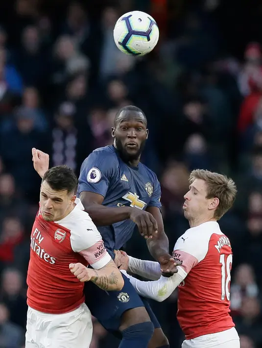 Striker Manchester United, Romelu Lukaku berebut bola dengan dua pemain Arsenal Granit Xhaka dan Nacho Monreal selama pertandingan lanjutan Liga Inggris di Stadion Emirates di London (10/3). Arsenal menang 2-0 atas MU. (AP Photo/Tim Ireland)