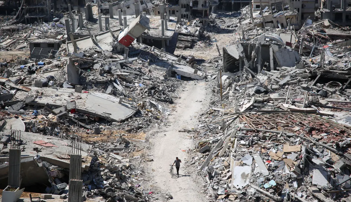Seorang pria mendorong sebuah sepeda sambil berjalan di antara reruntuhan bangunan di daerah yang hancur di sekitar rumah sakit Al-Shifa di Gaza pada 3 April 2024. (Foto oleh AFP)