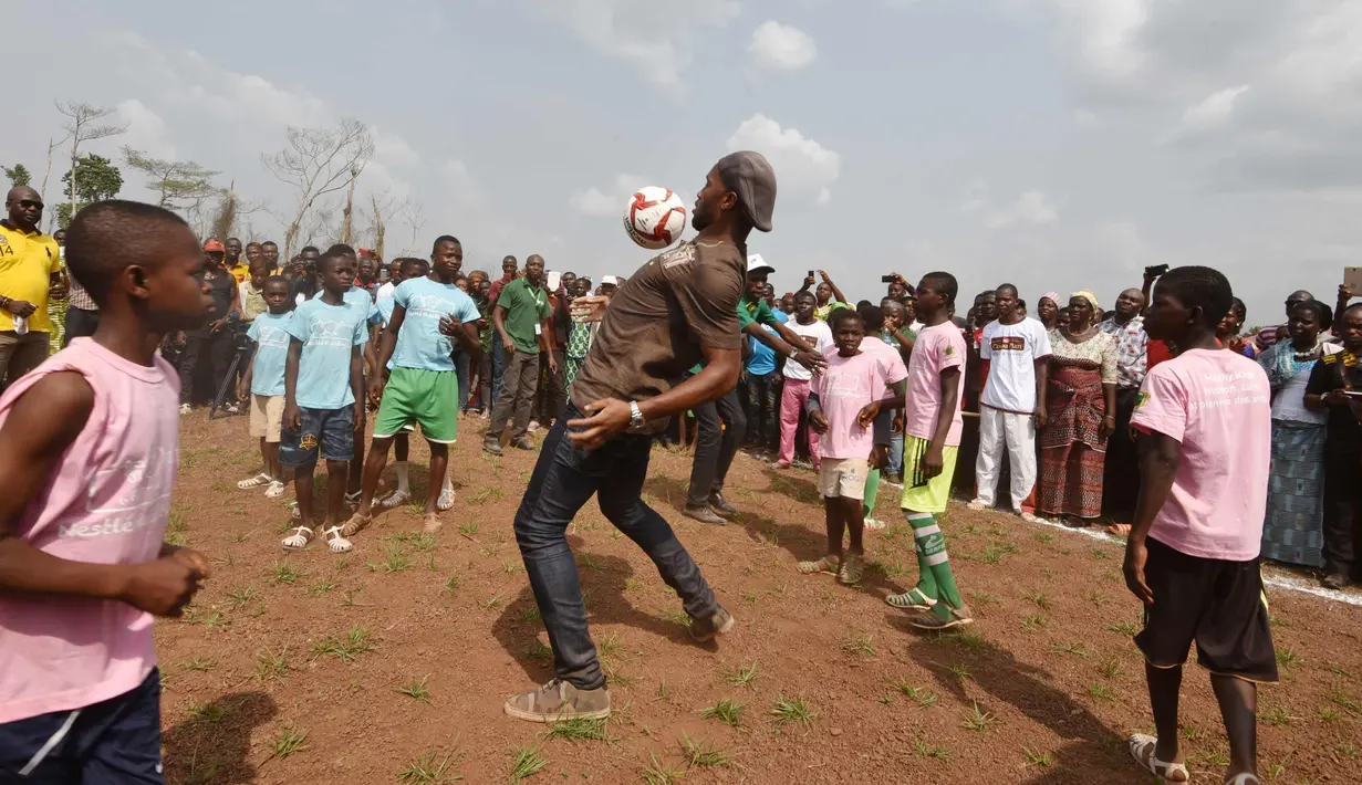 Mantan penyerang Chelsea, Didier Drogba berusaha mengontrol bola saat bermain dengan murid-murid saat peresmian sekolah di Pokou-Kouamekro, dekat Gagnoa, Pantai Gading tengah barat (17/1). (AFP Photo/Sia Kambou)