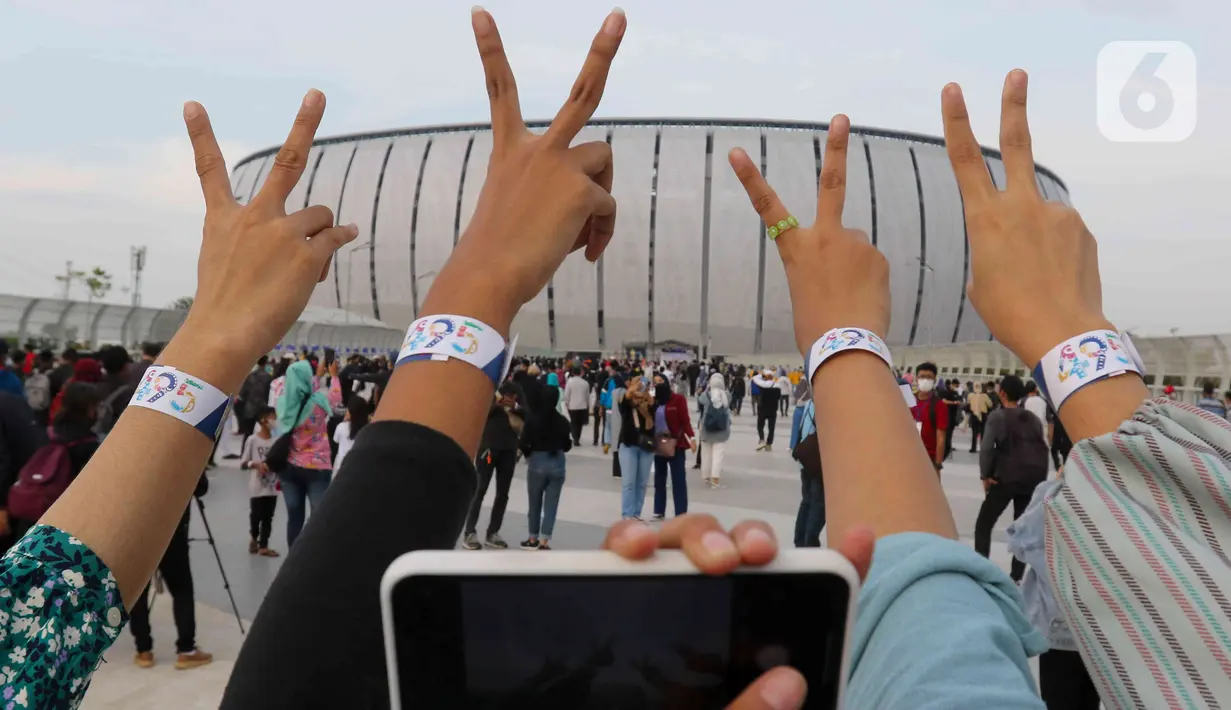 Sejumlah orang berfoto sambil menunjukkan gelang akses masuk acara hari ulang tahun (HUT) ke-495 DKI Jakarta atau Jakarta Hajatan di Jakarta International Stadium (JIS), Jakarta Utara, Sabtu (25/6/2022) malam. Seperti diketahui, Pemerintah Provinsi (Pemprov) DKI membuka secara gratis bagi masyarakat yang ingin memiliki tiket masuk. (Liputan6.com/Herman Zakharia)