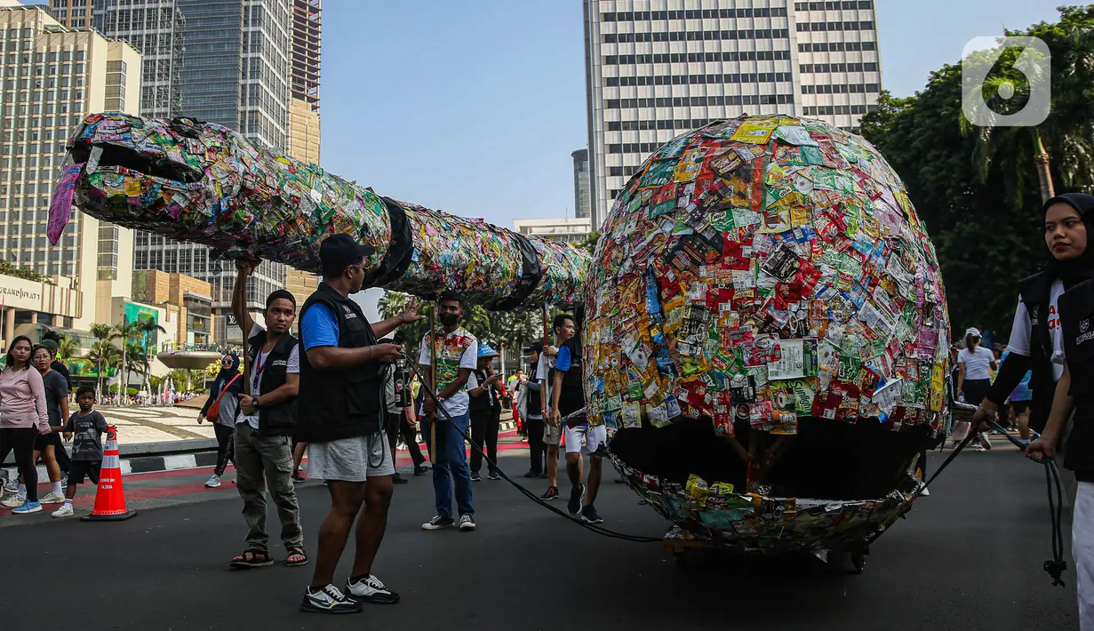 Aktivis lingkungan dari komunitas Aksi Muda Jaga Iklim berpawai dengan membawa replika ikan paus dan ular raksasa yang terbuat dari sampah plastik di kawasan Bundaran Hotel Indonesia, Jakarta, Minggu (27/10/2024). (Liputan6.com/Angga Yuniar)