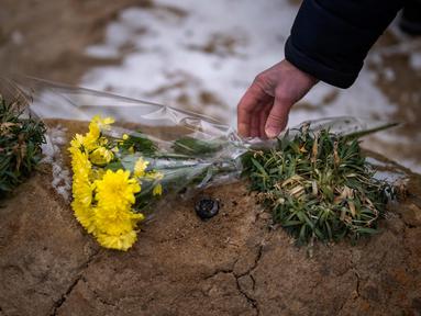 Seorang pria meletakkan bunga di makam seorang kerabatnya dalam upacara peringatan satu tahun dimulainya perang Rusia-Ukraina, di sebuah pemakaman di Bucha, Ukraina, Jumat, 24 Februari 2023. (AP Photo/Emilio Morenatti)