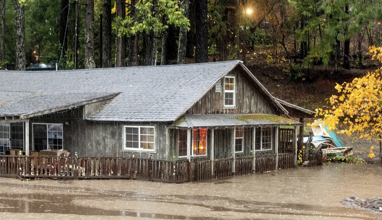 Banjir dari Danau Madrone mengalir melewati sebuah rumah di Oro Quincy Highway di Butte County, California, Minggu (24/10/2021). Badai kuat menerjang California Utara yang sempat mengalami kebakaran hutan, memicu tanah longsor dan banjir, juga membawa angin kencang. (AP Photo/Noah Berger)